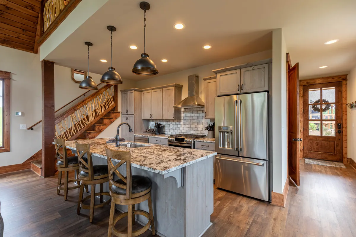 A view into the home's kitchen area featuring an island countertop, stainless steel appliances, a wooden staircase, and expansive windows. The space is ideal for cooking together, casual dining, and creating memories during festive gatherings.