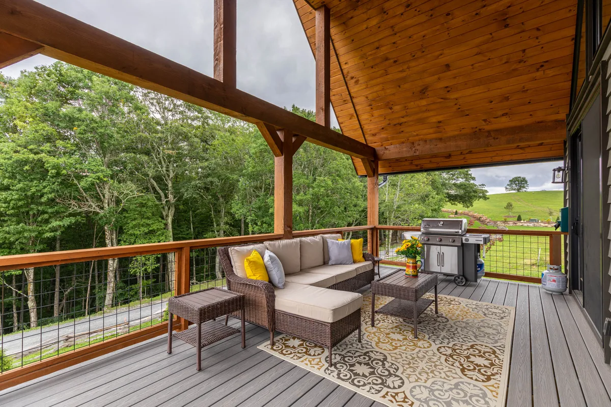 An inviting outdoor seating area with a grill, colorful decorative rug, and lush greenery all around. The patio offers a relaxed atmosphere for barbecues, morning coffee, and connecting with nature, with views extending into the natural surroundings.